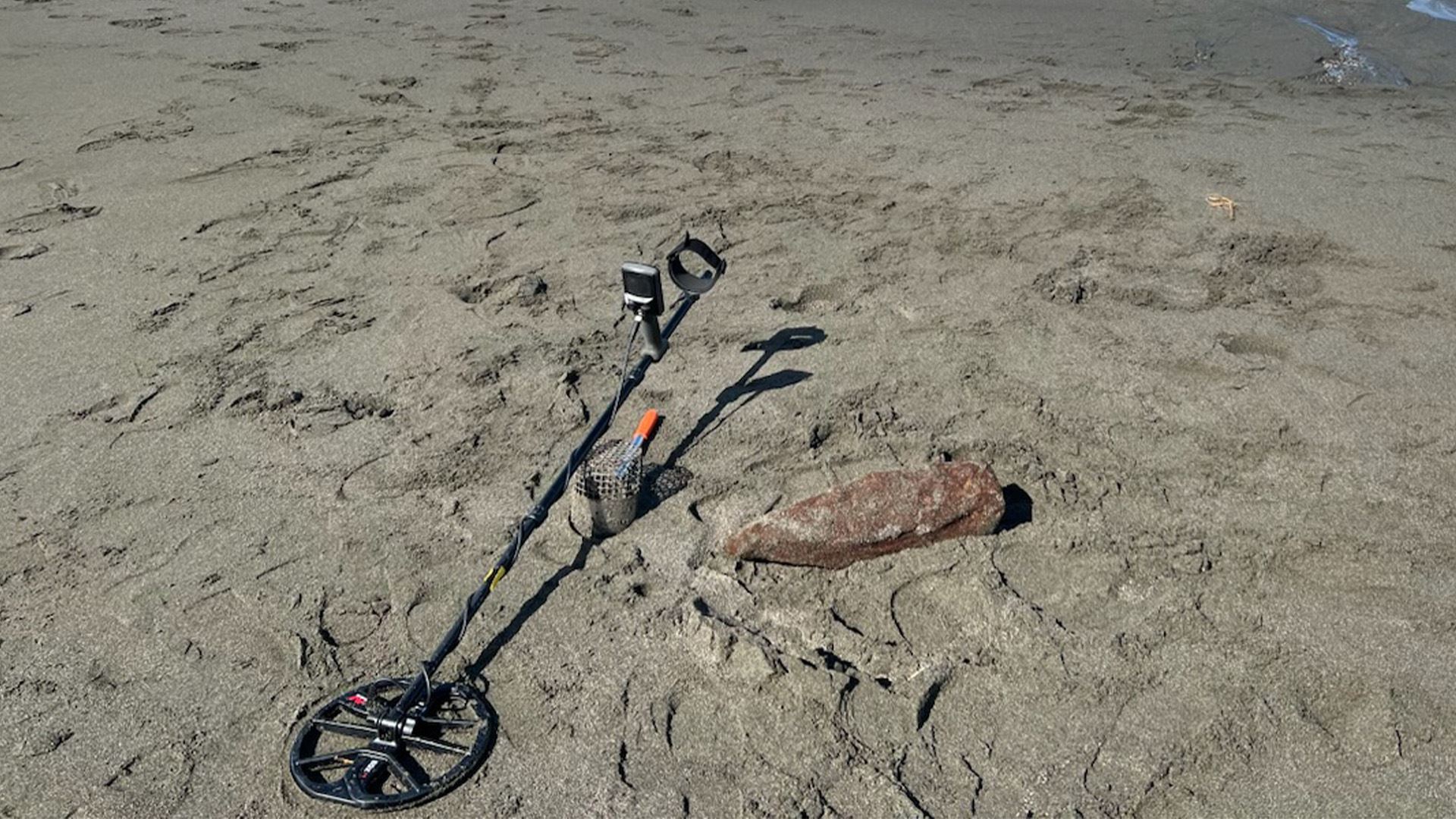 Antique military-grade artillery round and a metal detector on the beach.