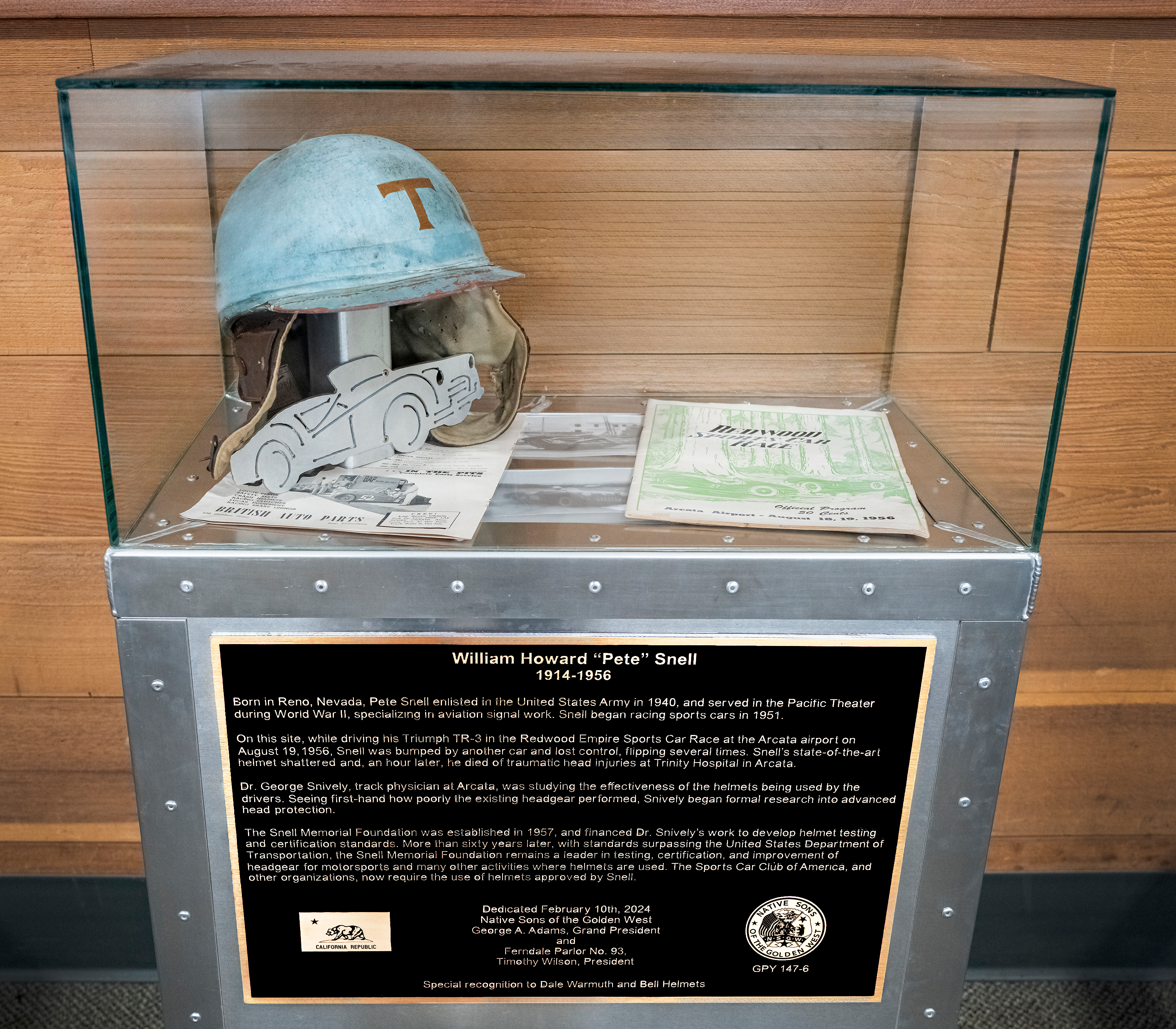 A glass case displaying a replica of William Howard “Pete” Snell’s 1956 racing helmet.