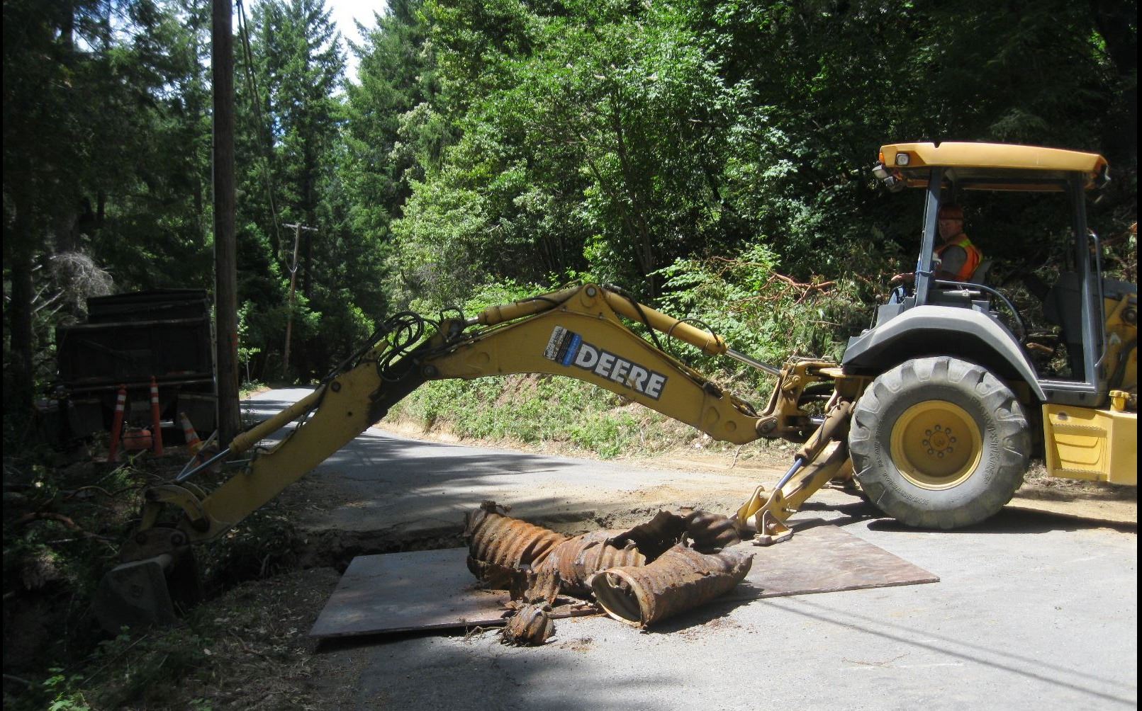 Heavy equipment digging a trench and replacing a damaged culvert