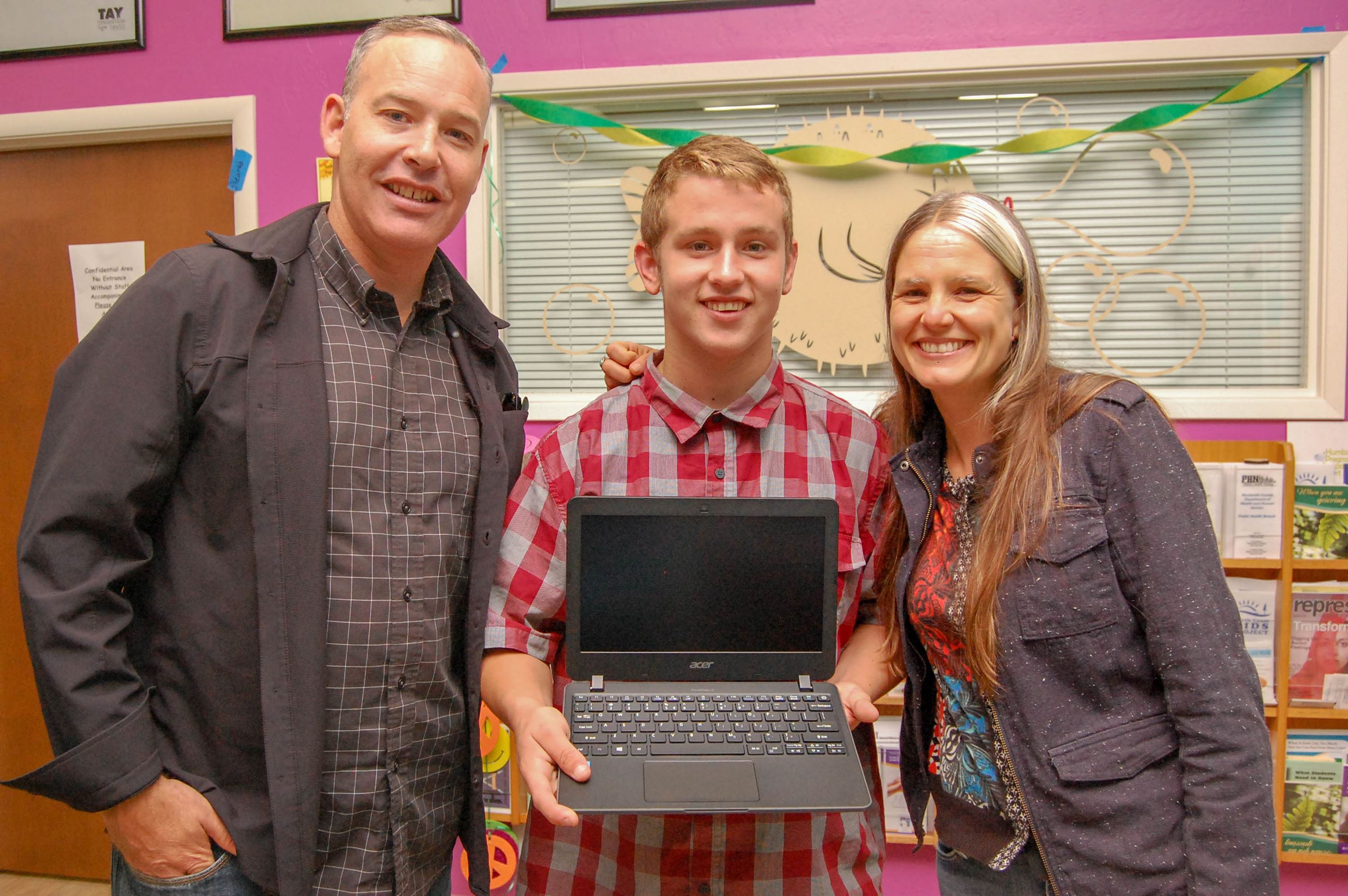 Foster youth holding a laptop standing between two support staff