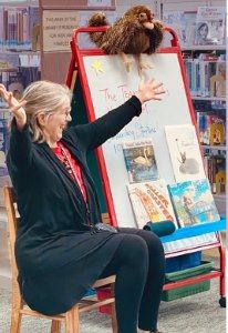 Ms. Sue flings her arms wide, hands open like stars, while telling a story.