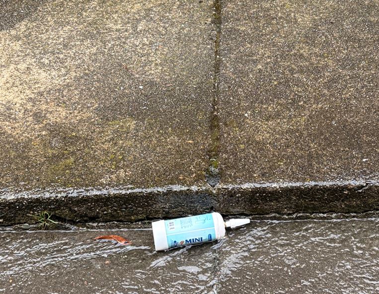 This picture shows a medium-sized nitrous oxide tank laying in run-off water on the road next to a sidewalk in a local neighborhood in Humboldt.