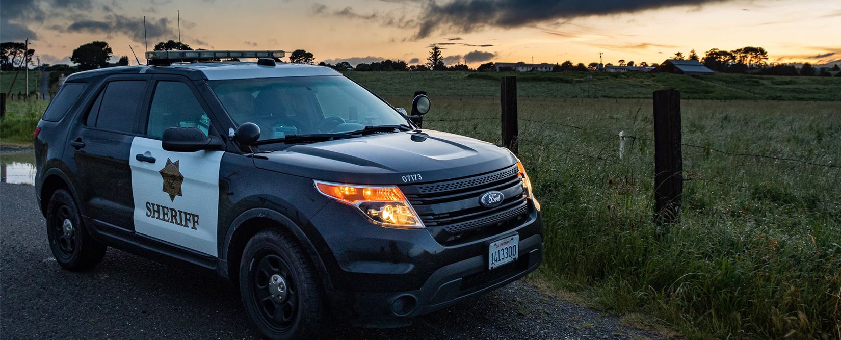 Sheriff’s patrol car parked in front of a field during sunset